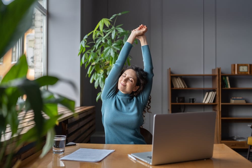 A woman practices yoga indoors, holding a side plank pose with one arm raised, in a sunlit studio with large windows - Chiropractor Meridian Idaho
